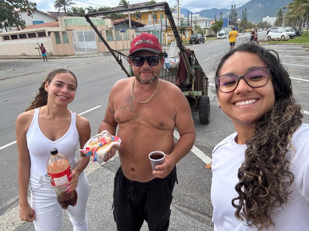 Selfie com um homem ao lado da carroça de reciclagem, segurando lanches e um copo de refrigerante